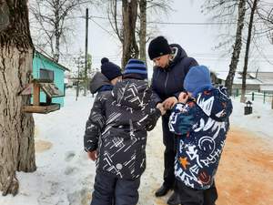 Подготовительная к школе группа "Пчёлки". Педагог Кондрашова Т.В. с воспитанниками насыпают семечки в птичьи кормушки во время прогулки.